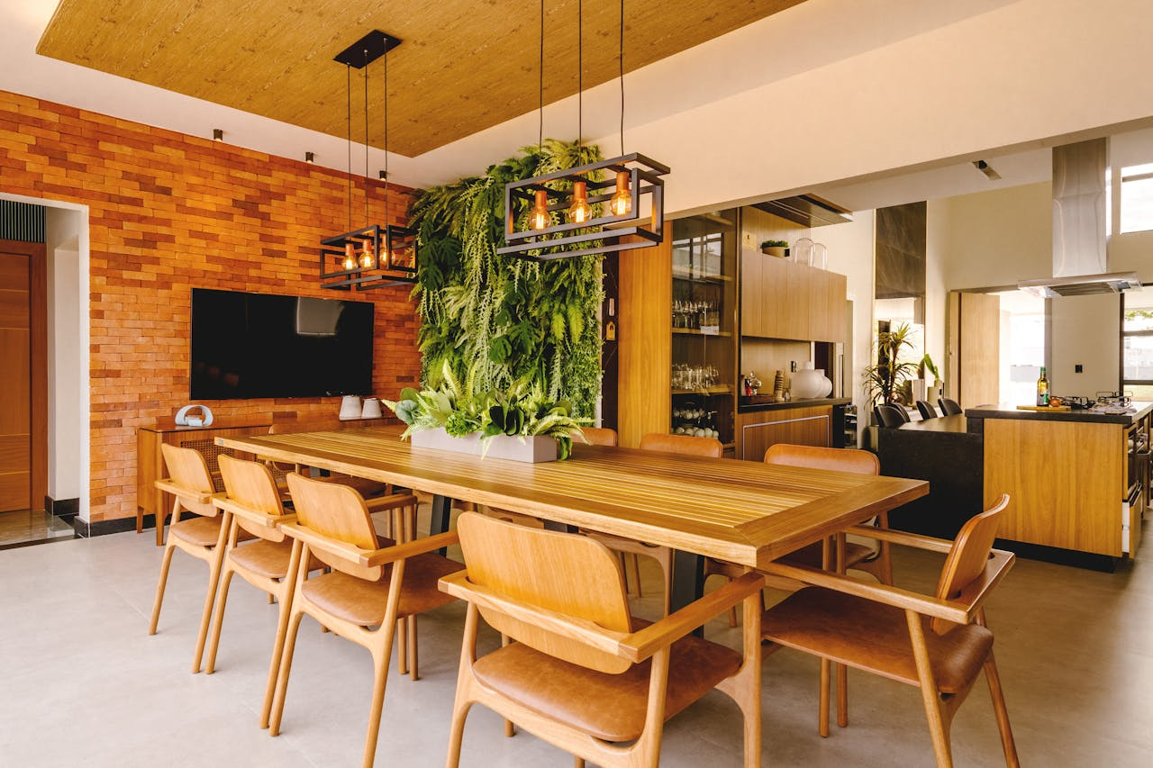 A stylish dining room featuring a wooden table, hanging greenery, and brick wall decor.