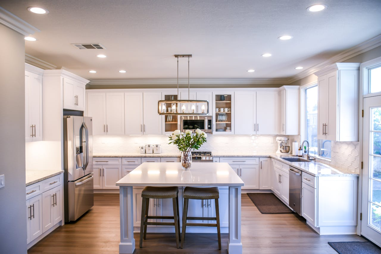 our-journey-01 Spacious and elegant kitchen featuring white cabinetry, island, and stainless steel appliances.