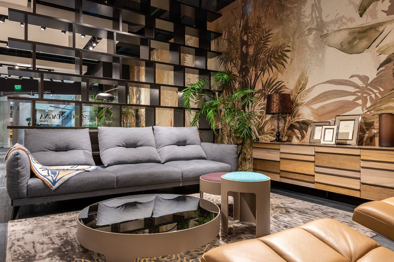 Stylish living room featuring a plush sofa, mirrored table, and tropical-themed wallpaper.