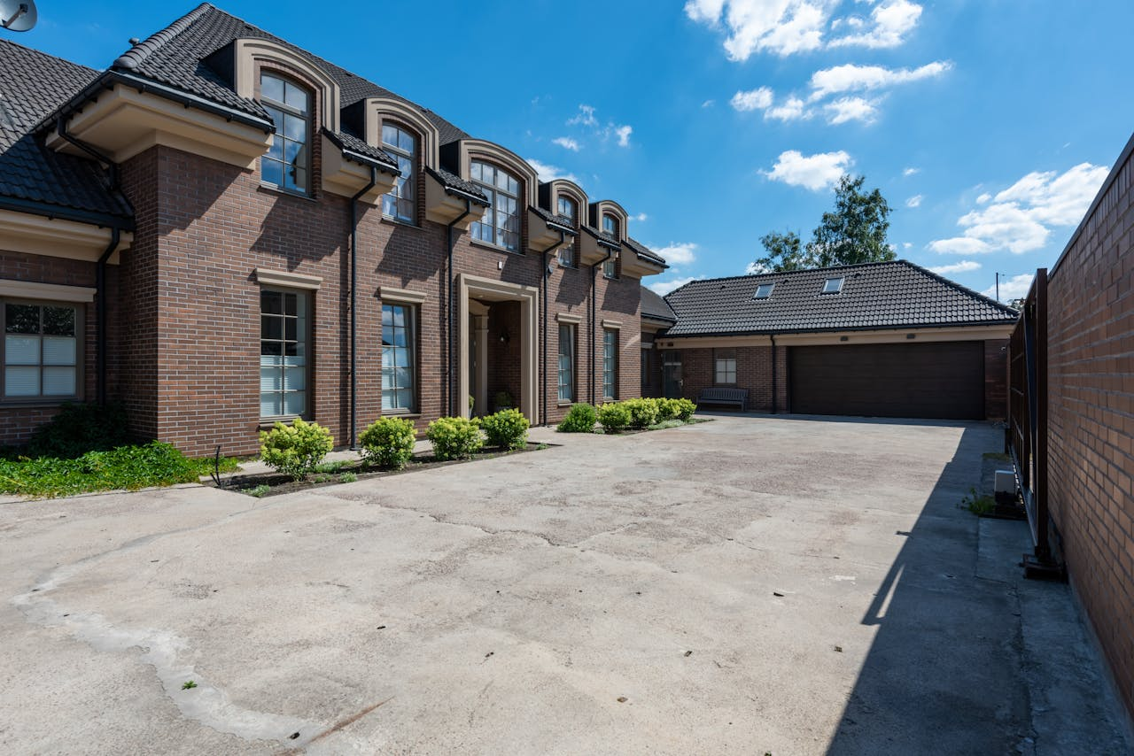 our-journey-02 Elegant brick house exterior with a large driveway under a clear blue sky.
